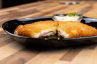 Fried Cheese with Ham Halved Fried Cheese with Ham showing melted cheese and ham inside crispy breading, on a black plate.
