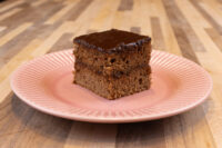 Gingerbread Bars Square Gingerbread Bars slice with dark preserve filling and chocolate glaze on a pink plate.