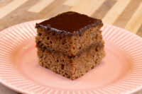 Gingerbread Bars Square Gingerbread Bar with dark chocolate coating and two visible layers, on a pink ridged plate.