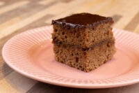 Gingerbread Bars A square Gingerbread Bar with dark chocolate glaze, showing two spiced cake layers, on a pink plate.