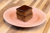 Gingerbread Bars Square Gingerbread Bar with dark chocolate coating and two cake layers, on a pink ridged plate.