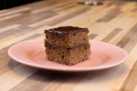 Gingerbread Bars A square Gingerbread Bars slice with dark chocolate coating and a filling layer, on a pink ridged plate.