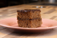 Gingerbread Bars Two stacked squares of Gingerbread Bars topped with glossy chocolate coating, on a pink ridged plate.