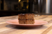 Gingerbread Bars A square of Gingerbread Bars with a dark glossy coating, stacked in two layers on a pink plate.