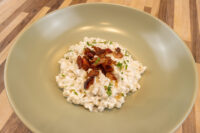 Halušky with Bryndza Cheese Substitution topped with crispy bacon and herbs on a sage-green plate.