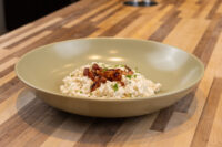 Bowl of Halušky with Bryndza Cheese Substitution topped with crispy browned bits and chopped herbs on a wooden table.
