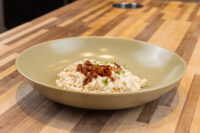 Bowl of Halušky with Bryndza Cheese Substitution, creamy dumplings topped with crispy bacon and herbs on a wood table.