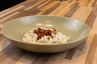 Halušky with Bryndza Cheese Substitution in a pale green bowl, topped with crispy bacon and herbs, on a wooden table.