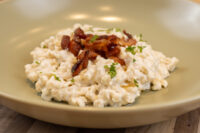 Halušky with Bryndza Cheese Substitution Halušky with Bryndza Cheese Substitution, creamy potato pasta topped with crispy bacon and herbs on a beige plate