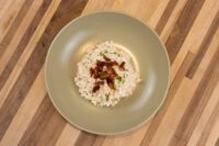 Halušky with Bryndza Cheese Substitution Halušky with Bryndza Cheese Substitution in a green bowl, topped with crispy bacon and herbs.
