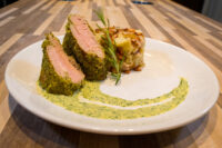 Herb-crusted Pork Tenderloin Sliced Herb-crusted Pork Tenderloin with pink center beside a potato bake and green herb sauce.