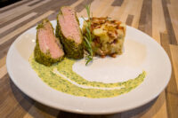 Herb-crusted Pork Tenderloin Sliced Herb-crusted Pork Tenderloin with pink centre beside a potato cake and green herb sauce.