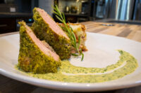 Herb-crusted Pork Tenderloin Sliced Herb-crusted Pork Tenderloin with pink center, green herb crust, rosemary garnish, and herb sauce swirl.