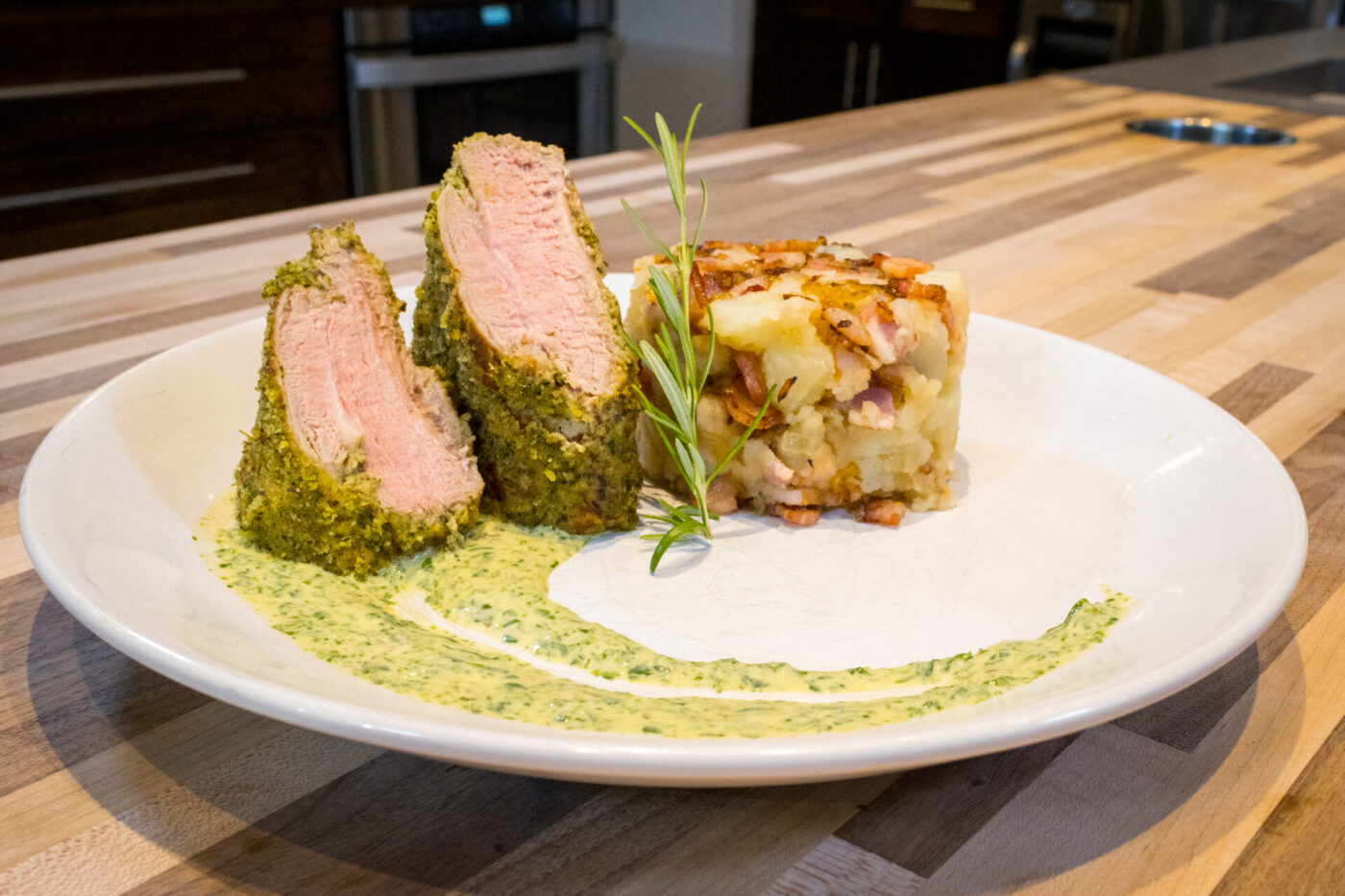 Herb-crusted Pork Tenderloin Sliced Herb-crusted Pork Tenderloin with pink center, herb sauce swirl, rosemary sprig, and potato-bacon hash