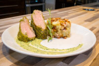 Herb-crusted Pork Tenderloin Sliced Herb-crusted Pork Tenderloin with pink center, herb sauce swirl, rosemary sprig, and potato-bacon hash