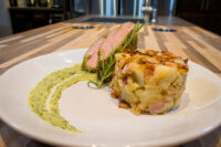 Herb-crusted Pork Tenderloin Sliced Herb-crusted Pork Tenderloin with rosemary, potato-bacon cake, and green herb sauce on a white plate.