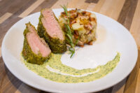 Herb-crusted Pork Tenderloin Sliced Herb-crusted Pork Tenderloin with pink centers beside roasted potatoes and herb sauce.