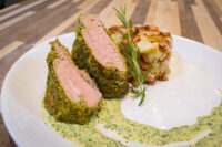 Herb-crusted Pork Tenderloin Sliced Herb-crusted Pork Tenderloin with pink center, roasted potatoes, rosemary, and green herb sauce on a white plate