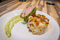 Herb-crusted Pork Tenderloin Sliced Herb-crusted Pork Tenderloin with herb crust edge, beside a potato-bacon cake and herb sauce swirl