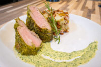 Herb-crusted Pork Tenderloin Sliced Herb-crusted Pork Tenderloin with pink center beside roasted potatoes and green herb sauce
