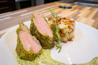 Herb-crusted Pork Tenderloin Sliced Herb-crusted Pork Tenderloin with pink centre in green herb sauce, beside a potato bake