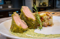 Herb-crusted Pork Tenderloin Sliced Herb-crusted Pork Tenderloin with pink centres, plated beside a potato bake and green herb sauce