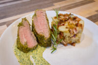Herb-crusted Pork Tenderloin Sliced Herb-crusted Pork Tenderloin with pink centre, green herb sauce, potatoes and bacon, rosemary sprig