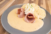 Horseradish Sauce Křenová Omáčka pooled on a plate with rolled ham, whipped cream, and biscuits