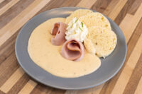Horseradish Sauce Křenová Omáčka pooled on a plate with folded ham, whipped cream, and biscuits