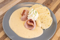 Creamy Horseradish Sauce Křenová Omáčka pooled on a plate with rolled ham slices and whipped cream garnish