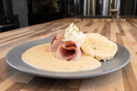 Horseradish Sauce Křenová Omáčka pooled on a gray plate with rolled ham, a biscuit, and a chive-topped dollop.