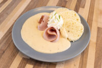 Horseradish Sauce Křenová Omáčka pooled on a plate beside rolled smoked ham and a cream garnish