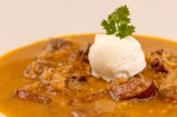 Bowl of Kapustnica Soup with meat and sausage chunks, topped with cream and a parsley sprig.