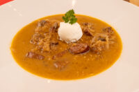 Bowl of Kapustnica Soup with mushrooms, sausage, a cream dollop, and parsley garnish.