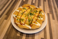 Langos Round fried Langos flatbread topped with cheese, white and red drizzle, and chives on a white plate
