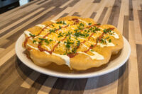 Langos Langos flatbread topped with melted cheese, sour cream, red sauce, and chives on a white plate.