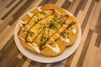 Langos Fried Langos flatbread on a plate with red sauce, sour cream drizzle, shredded cheese, and chives