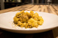 Mac & Cheese Plated Mac & Cheese topped with golden toasted breadcrumbs on a white dish over a wooden table