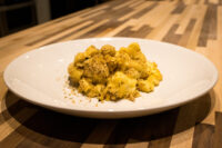 Mac & Cheese White plate of baked Mac & Cheese with a golden herb crumb topping on a wooden table.