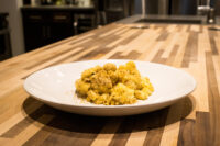 Mac & Cheese White plate of Mac & Cheese with creamy sauce and golden herb crust on a wooden counter.