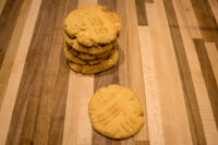 Peanut Butter Cookies Stack of Peanut Butter Cookies with fork-tine crosshatch marks, one cookie set beside the stack on a wooden board.