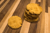 Peanut Butter Cookies A stack of Peanut Butter Cookies with fork crosshatch marks beside one single cookie on a striped wood surface.