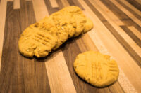 Peanut Butter Cookies Five crosshatch-topped Peanut Butter Cookies with peanut flecks on a striped wooden board