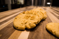 Peanut Butter Cookies A Peanut Butter Cookies with crosshatch fork marks and peanut flecks on a striped wooden board.
