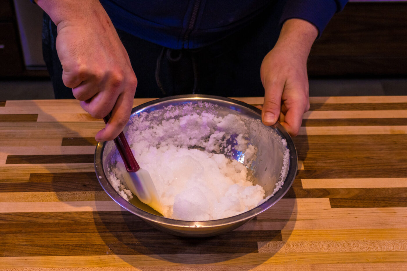 Hands stirring a wet-sand salt mixture in a steel bowl for Beef Picanha in Salt Crust.