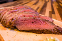 Beef Picanha in Salt Crust Sliced Beef Picanha in Salt Crust fanned out on a wooden cutting board, pink center visible.