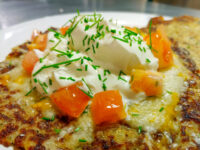 Potato Pancakes Bramboraky Golden Potato Pancakes Bramboraky topped with sour cream, diced tomato, and chives on a white plate.