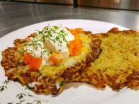 Potato Pancakes Bramboraky Two crisp Potato Pancakes Bramboraky topped with sour cream, diced tomato, melted cheese, and chives on a white plate.