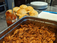 Pulled pork Pan of shredded pulled pork with a jar of BBQ sauce and biscuits on a cooling rack nearby.