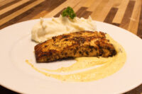 Salmon in Mustard Sauce Seared Salmon in Mustard Sauce with a blackened crust, mashed potato, and pale cream sauce on a white plate.
